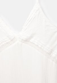 Haut en tissu blanc avec un décolleté en V orné de dentelle, motif texturé en côtes et bretelles délicates. Matière légère et respirante.