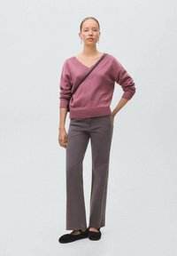 Roza pletena pulover s V-izrezom, združen z sivo širokimi hlačami. Obleka je dopolnjena s črnimi natikači in torbico čez ramo.