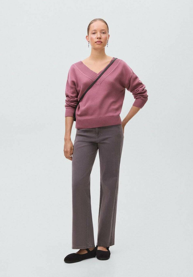 Roza pletena pulover s V-izrezom, združen z sivo širokimi hlačami. Obleka je dopolnjena s črnimi natikači in torbico čez ramo.