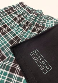 Szorty w kratkę w kolorze turkusowym, czarnym i białym z elastycznym paskiem w talii oraz czarna koszulka z etykietą logo "DOM & RELAKS OD 1989 R."