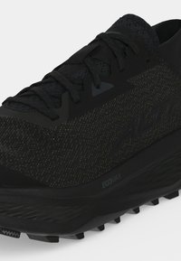 Chaussure de sport noire à lacets avec empeigne texturée, semelle épaisse avec l'inscription ECOMAX, et nom de la marque embossé sur le côté.