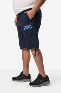 Pantaloni cargo navy con dettagli del logo, dotati di tasche laterali e orlo regolabile. Abbinati a scarpe da ginnastica nere con accenti grigi.