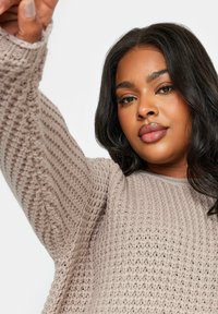 Maglione a maglia beige chiaro con texture a nido d'ape e maniche lunghe, caratterizzato da una vestibilità morbida e scollatura rotonda. Tessuto a fantasia visibile.