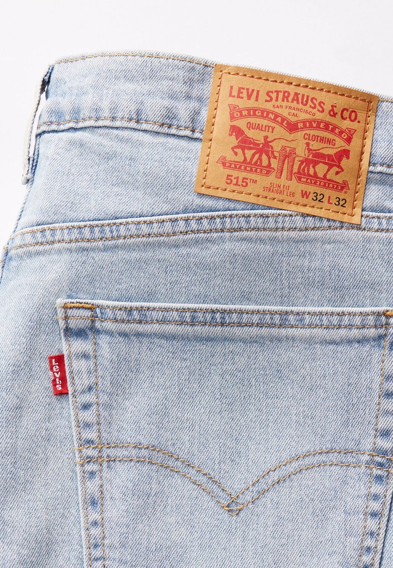 Lichtblauwe denim jeans met een bruine leren patch met rode en zwarte typografie, gele stiksels en een rode Levi's-tab op de zak.