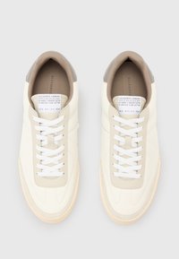Sneakers bianchi in pelle con una texture liscia, dettagli beige sul tallone e lacci bianchi. Presentano un design minimalista e una suola in gomma.