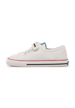 Zapatilla blanca de lona de corte bajo con cordones y tira de velcro, ribete rojo y suela de goma con rayas negras, vista lateral sobre fondo blanco.