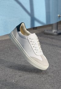 Sneaker in pelle bianca con punta in suede grigia e tallone blu scuro. Presenta lacci bianchi piatti e suola in gomma crema.