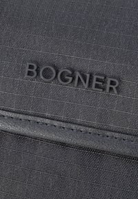 Bolsa textil negra con superficie texturizada, que presenta un destacado logo negro "BOGNER" y un borde de cuero en contraste a lo largo del borde.