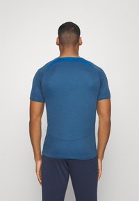Camiseta deportiva azul de manga corta con textura suave, con detalles en contraste en los hombros y un diseño entallado, vista desde atrás.