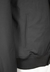 Schwarze Bomberjacke mit glatter Textur, elastischem Rippbund und einer seitlichen Reißverschlusstasche. Schlichtes und funktionales Design.