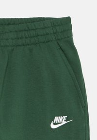 Zelene bombažne trenirke z elastičnim pasom, opremljene z stranskimi žepi in belim izvezenim logotipom Nike na sprednji strani.