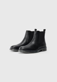 Bottines Chelsea en cuir noir avec une finition texturée, des panneaux latéraux élastiques et un petit talon empilé. Bout lisse et languette à l'arrière.