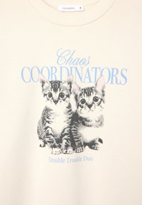 Felpa beige con una grafica di due gattini a strisce, con la scritta "Coordinatori del Caos" in blu e "Duo di Doppia Problematica" sotto.