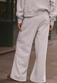 Graue weite Sweatpants aus dickem Baumwollgewebe, mit einer Gesäßtasche und einer lässigen Passform, kombiniert mit braunen Schuhen und schwarzen Sonnenbrillen.