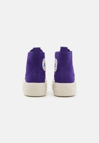Purple high-top sneakers made of suede with a textured finish, featuring a logo patch and a cream-colored rubber sole.