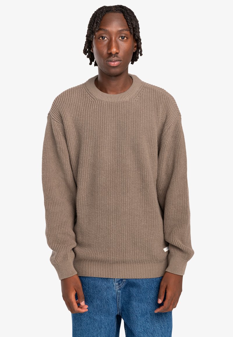 Bruine gebreide trui met een geribbeld textuur, ronde hals en een oversized pasvorm. Gepaard met blauwe jeans, met een casual en ontspannen ontwerp.