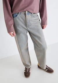 Lys blå denim jeans med avslappet passform, med knappestang, fem lommer og lett falming. Brukt med brune joggesko.