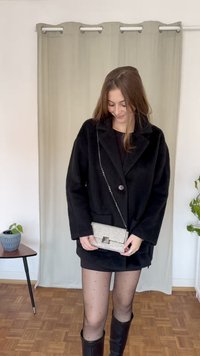 Abrigo negro de gran tamaño con un solo botón, combinado con un vestido mini negro, medias de lunares y botas marrones hasta la rodilla. Sosteniendo un clutch con tachuelas.