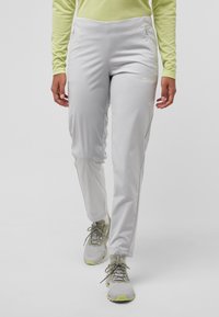 Lichtgrijze outdoorbroek met een flexibele pasvorm, zijzakken en ritsopeningen; gedragen met grijze en limoen sneakers, gecombineerd met een lichtgroen shirt.