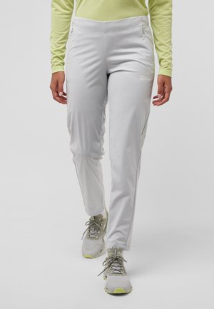 Lichtgrijze outdoorbroek met een flexibele pasvorm, zijzakken en ritsopeningen; gedragen met grijze en limoen sneakers, gecombineerd met een lichtgroen shirt.