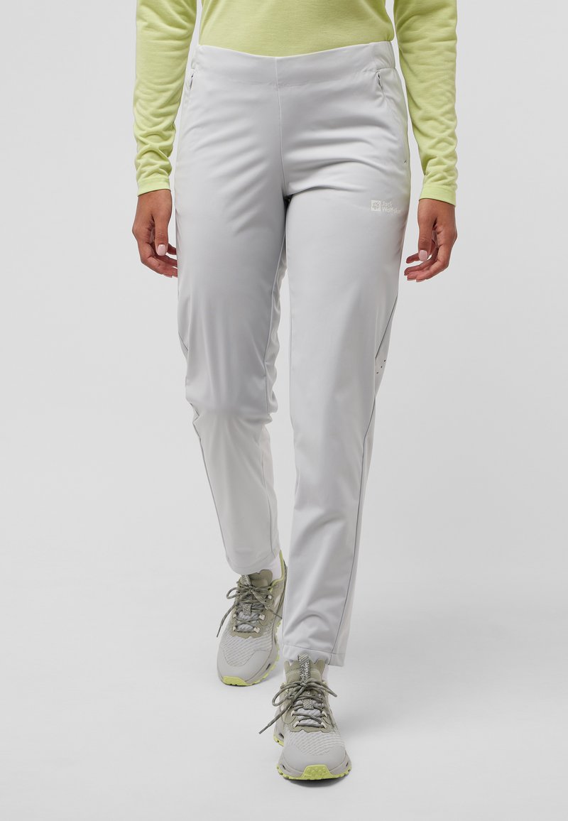 Lichtgrijze outdoorbroek met een flexibele pasvorm, zijzakken en ritsopeningen; gedragen met grijze en limoen sneakers, gecombineerd met een lichtgroen shirt.