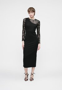 Mustmust mustrüübis, kus on pikad pitskäised, rõhutatud figuuri ja tekstuuriga lillemustriga käised. Sile kangas kehale.