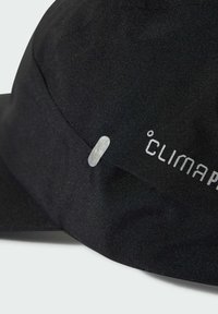 Primer plano de una tela negra con una pequeña tira reflectante y texto gris "CLIMAPROOF" impreso.