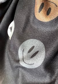 Tessuto nero con faccine sorridenti stampate in grigio e marrone. Texture morbida con un aspetto leggermente marmorizzato. Il design presenta caratteristiche semplici ed espressive.