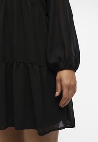 Robe noire transparente avec des manches bouffantes, taille froncée et ourlet en couches. Tissu doux et fluide avec une texture lisse.