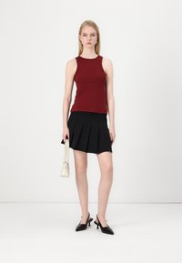 Burgundy sleeveless top paired with a black pleated skirt, black slingback heels, and a small white handbag. Minimalist design, smooth textures.