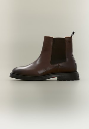 Brauner Leder-Chelsea-Stiefel mit schwarzem elastischem Seitenpanel und dicker schwarzer Sohle auf schlichtem hellem Hintergrund.