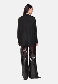 Schwarzes Langarmshirt mit plissiertem Rückendetail, kombiniert mit glänzenden, weit geschnittenen metallischen Hosen. Glatte Textur und elegante Silhouette hervorgehoben.