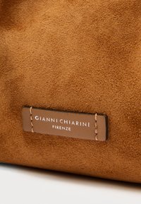 Barna színű, sima tapintású, kötött varrású velúr táska. Bőr címkéjén a "GIANNI CHIARINI FIRENZE" felirat dombornyomott formában.