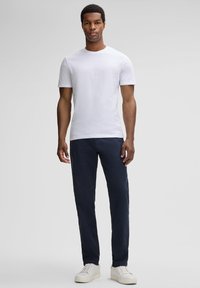 Maglietta bianca a maniche corte abbinata a pantaloni blu scuri e sneakers bianche, con un semplice colletto rotondo e un design dalla vestibilità rilassata.