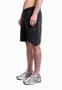 Calções pretos de algodão com cintura elástica e bolsos laterais. Usados com sapatilhas cinzentas com detalhes a preto e branco.