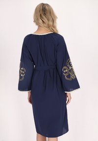 Rochie bleu marin cu mâneci lungi, evazate. Prezintă broderie aurie pe mâneci și un tiv texturat. Include o talie cu șiret și un decolteu rotund.