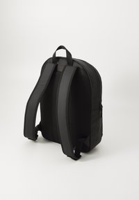 Zaino nero con forma arrotondata, realizzato in materiale liscio, dotato di spallacci in rete imbottita e di una maniglia superiore per una facile portabilità.