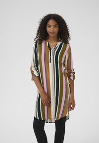 Tunique multicolore avec des rayures verticales vertes, brunes, roses, blanches et noires, avec un col en V et des manches retroussées. Tissu texturé.