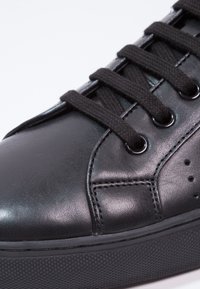 Baskets en cuir noir à finition lisse, avec des lacets noirs, des œillets ronds et une semelle en caoutchouc texturée. Détails de coutures subtiles.