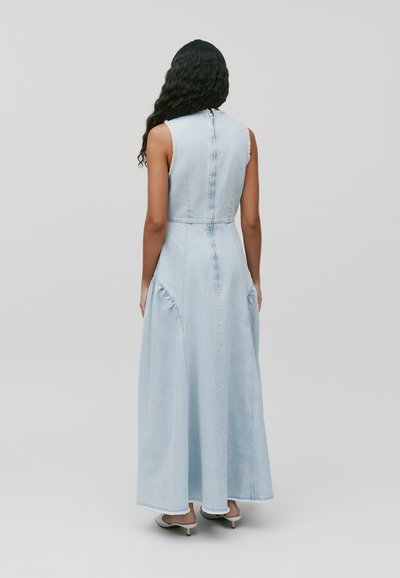 Robe maxi en denim bleu clair avec un design sans manches, fermeture éclair dans le dos et détails froncés sur les côtés. Texture lisse et silhouette fluide.