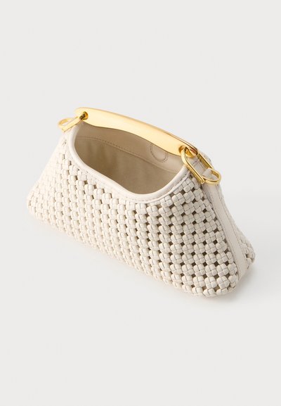 Λευκή υφαντή τσάντα με δομημένο σχήμα και καμπυλωτή χρυσή μεταλλική λαβή που ακουμπά σε φωτεινή επιφάνεια.