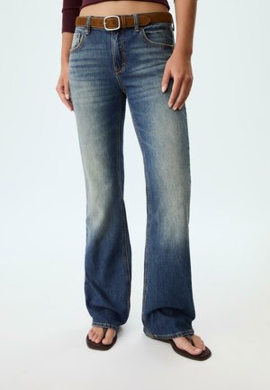 Blaue ausgestellte Denim-Jeans mit einer hellen Waschung, fünf Taschen und einem braunen Gürtel. Strukturierter Stoff mit sichtbaren Nähdetails und einer lockeren Passform.
