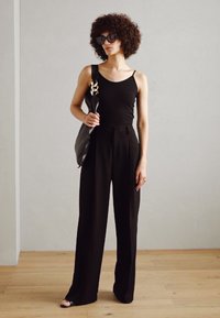 Black tank top, high-waisted black trousers with a wide leg, and a large black handbag with a gold strap detail. Smooth textures, minimalist design.