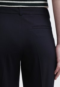 Pantaloni neri su misura con una texture liscia, dotati di una tasca posteriore e una vestibilità slim. Il tessuto è leggero e presenta una leggera lucentezza.