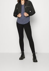 Černá bomber bunda s vroubkovanými manžetami, nošená přes námořnickou texturovanou polokošili, spárovaná s čern�ými skinny džíny a černými šněrovacími botami.