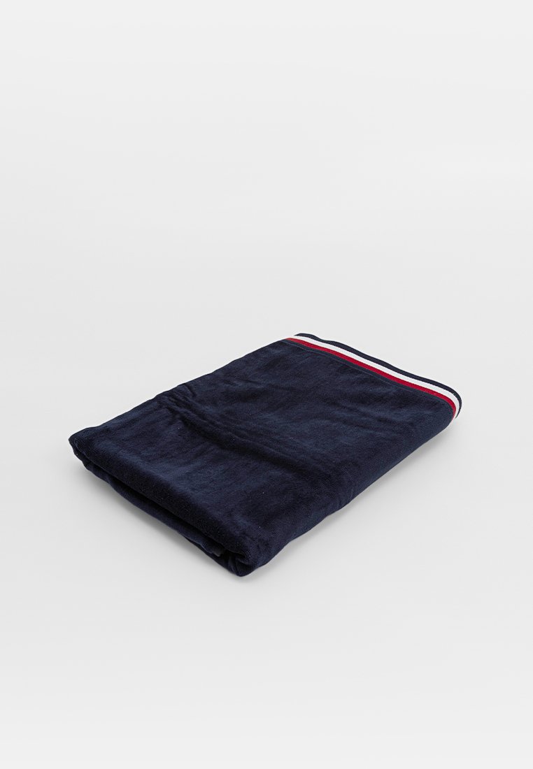 Toalla de color azul marino, de textura suave, doblada. Presenta un acento a rayas rojas y blancas en el borde. Apta para diversas tareas de secado.