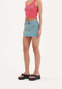 Rosa bauchfreies Tanktop mit glitzerndem Text, kombiniert mit einem hellblauen Jeans-Minirock mit blauen bestickten Details. Schwarze Plateausandalen.