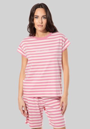 Frau mit dunklem Haar, die ein rosa-weiß gestreiftes kurzärmeliges Oberteil und passende Shorts trägt, mit dem Schriftzug "SHORT STORIES" auf dem Shirt.