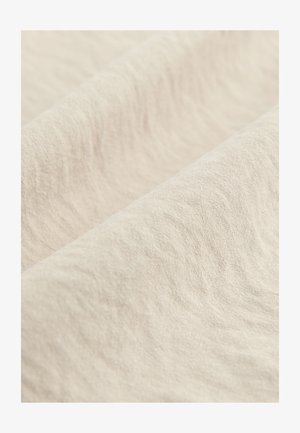 Vaaleanbeige kangas, jossa on hieman teksturoitu pinta, esittäen hienovaraisia aaltoja ja laskoksia, luoden pehmeän ja luonnollisen vaikutelman.