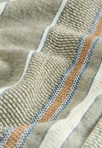 Textil in erdigen Tönen mit einer gewebten Textur und markanten Streifen in Beige, Blau und Rostfarben, die ein geschichtetes Aussehen erzeugen.
